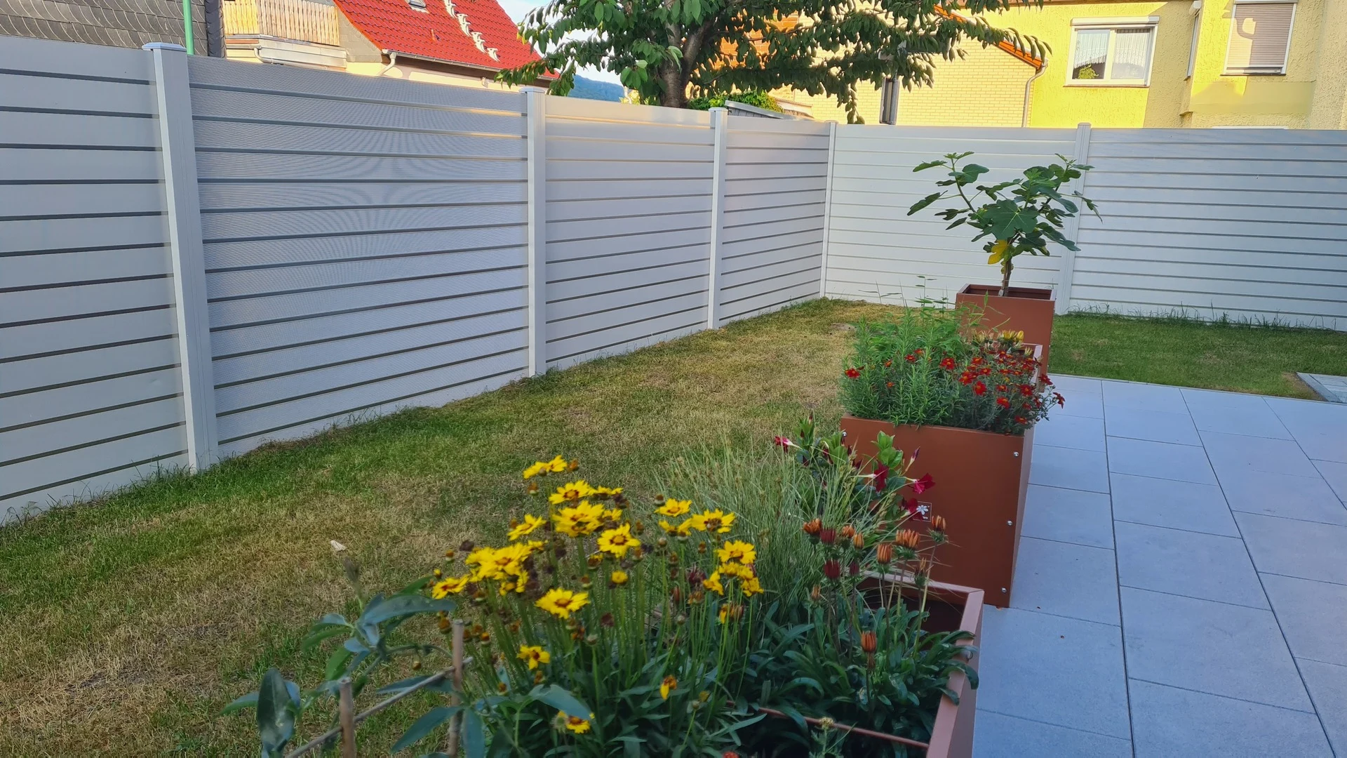 Blickdicht-Sichtschutz rund um einen Garten mit Terrasse und bl&uuml;henden Pflanzen